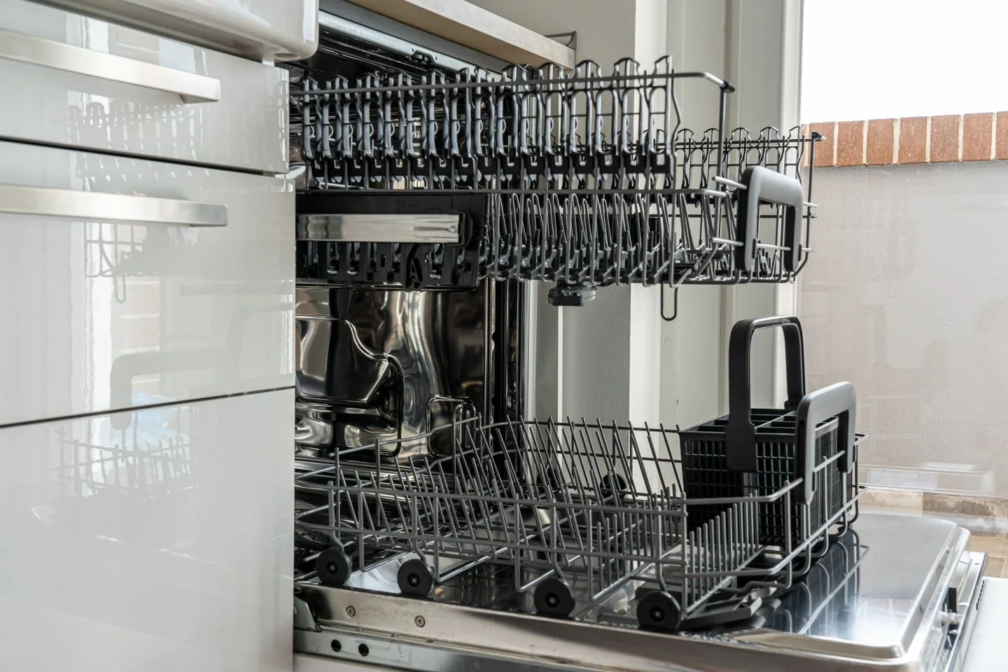An open empty dishwasher with racks in a kitchen.