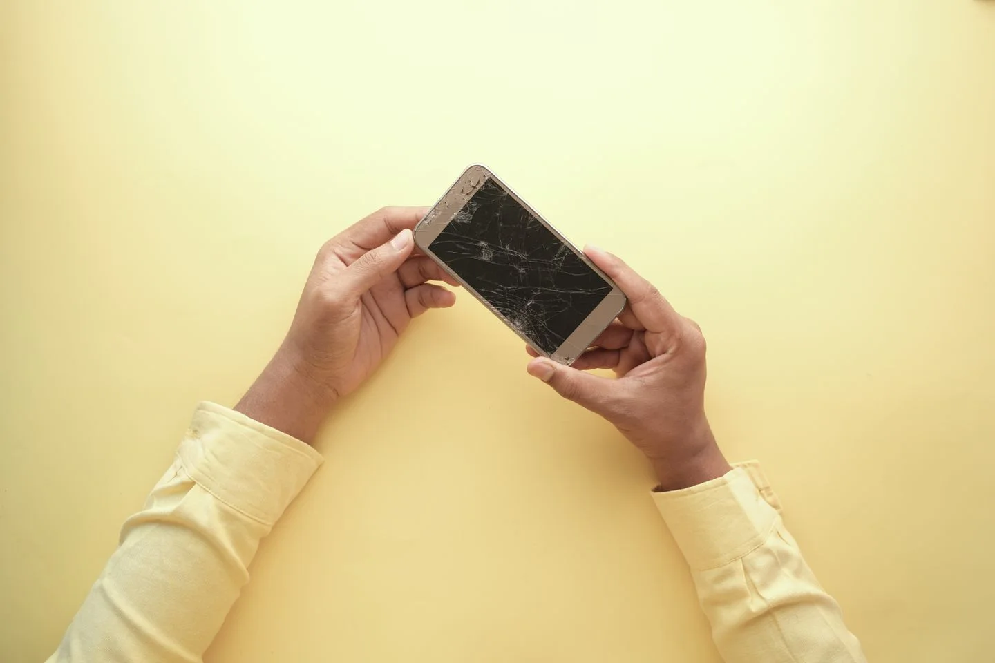 Hands holding a smartphone with a cracked screen.