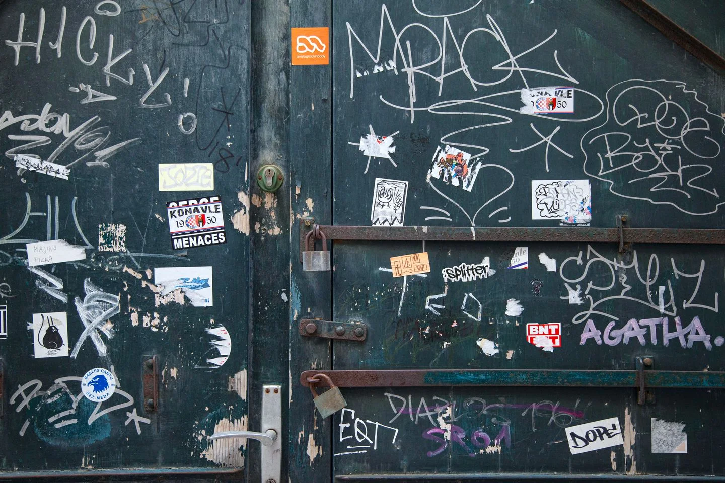 A weathered metal door with graffiti, stickers, and a lock.