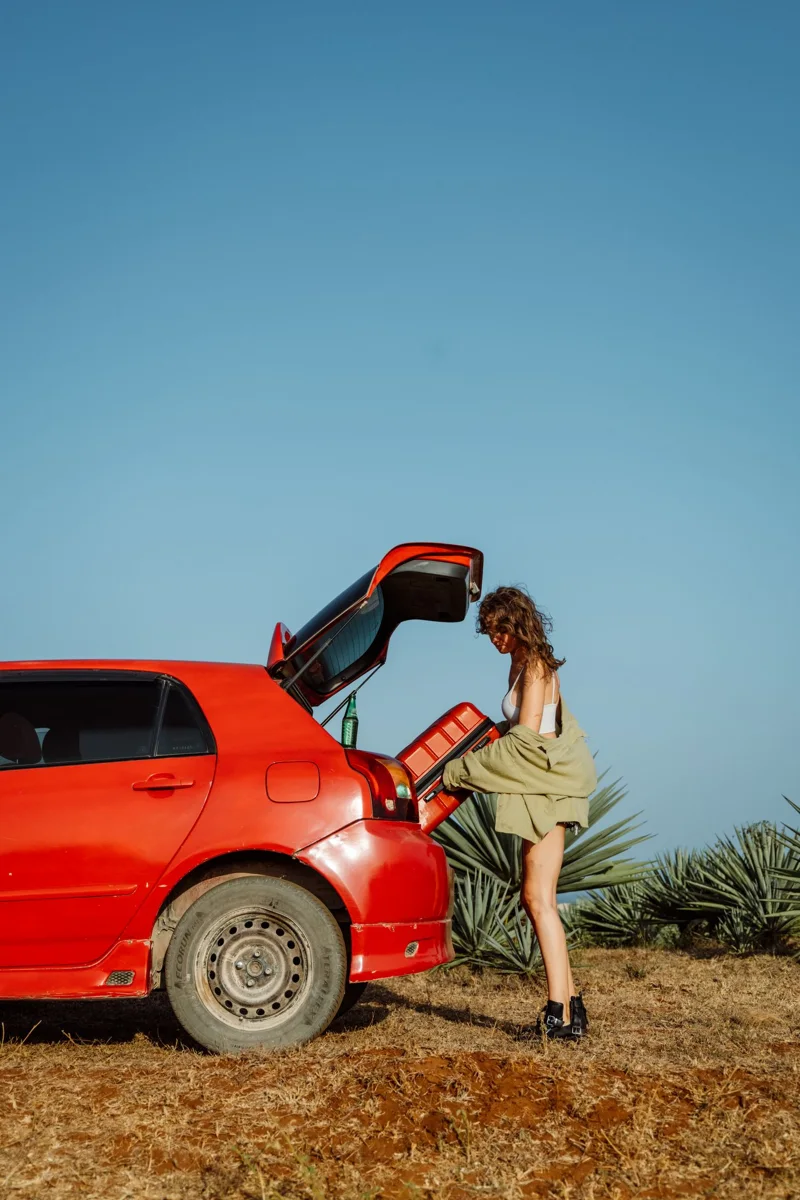 A woman placing a suitcase in a car's open boot.
