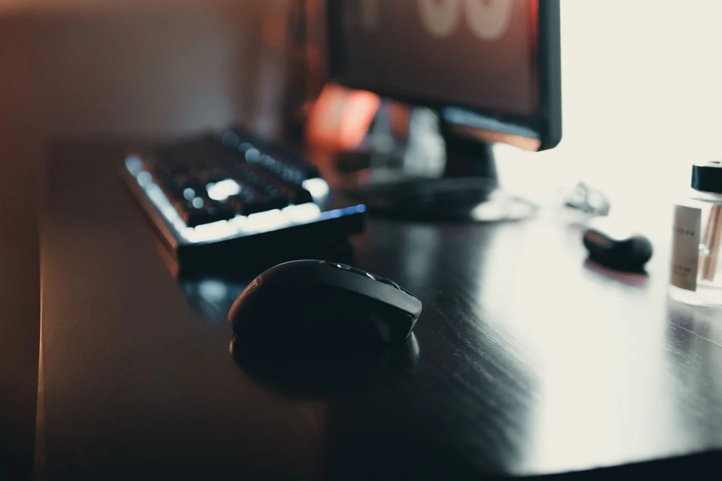 A monitor, keyboard, and black mouse on a wooden desk