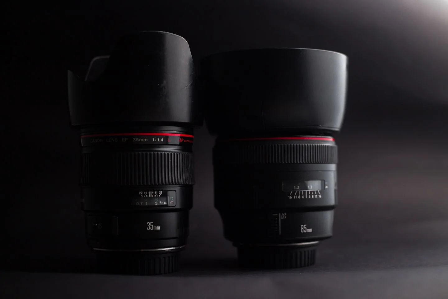 Two camera lenses stand together against a dark background