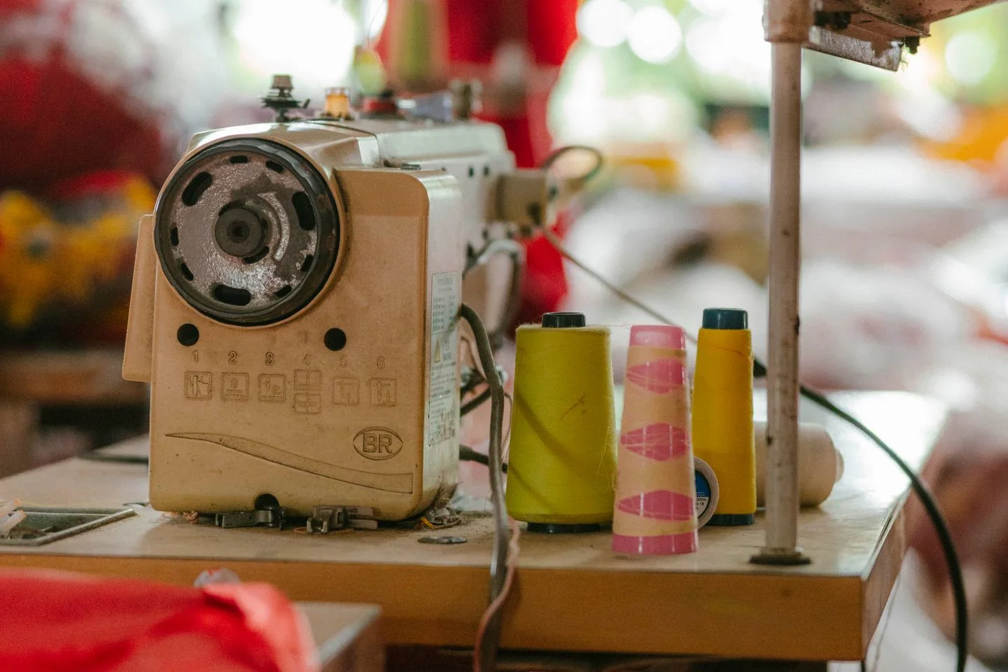 A sewing machine and colourful thread spools stand on a worktable