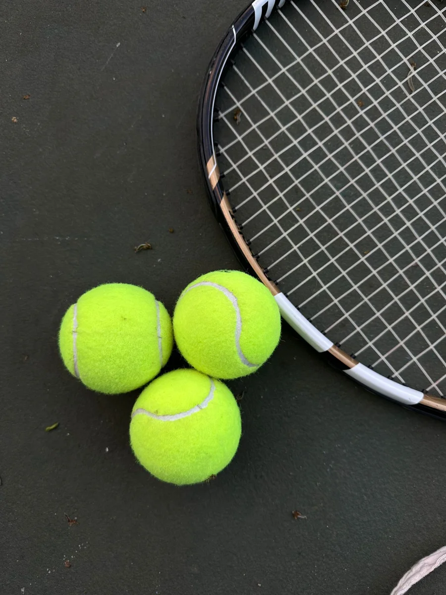 A tennis racket and tennis balls lie on a court