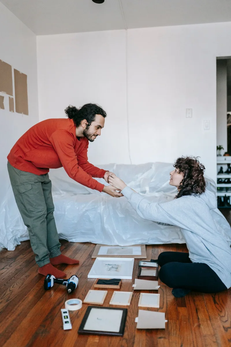 Two people arrange picture frames in a living room